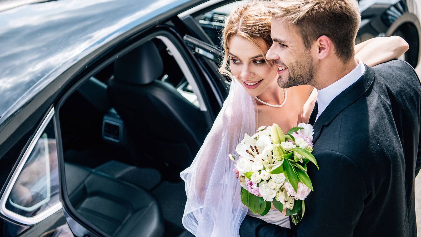 Image of a newly wed couple in a luxury vehicle being driven away.